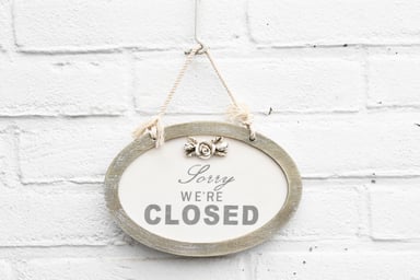 Sorry we're closed sign hung on a white brick wall