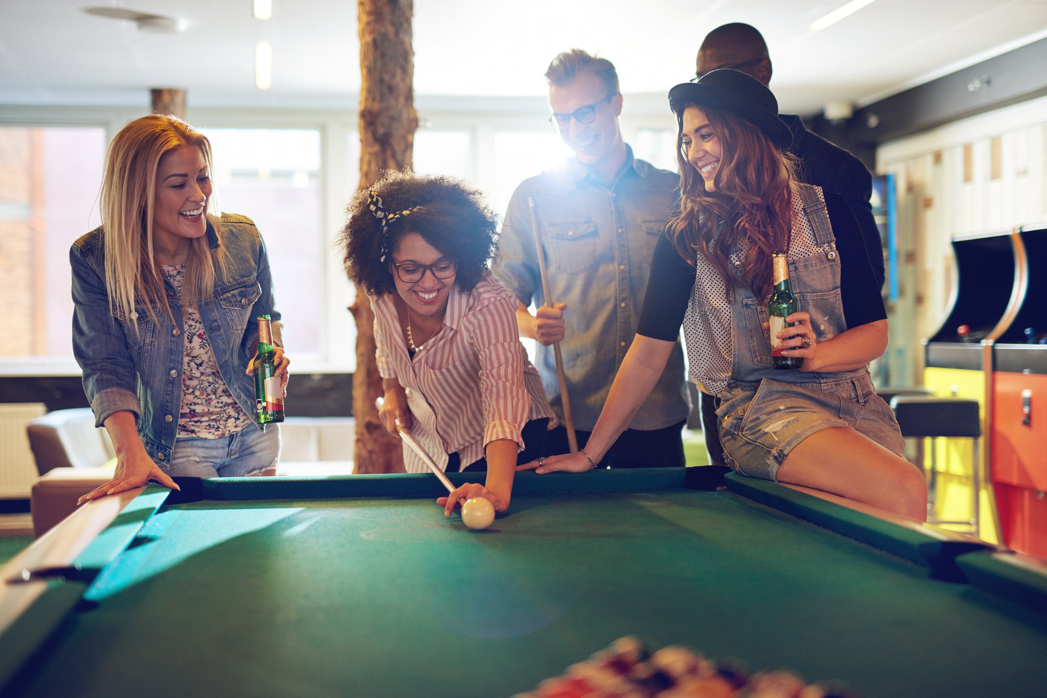 A group of people playing pool in an arcade. 