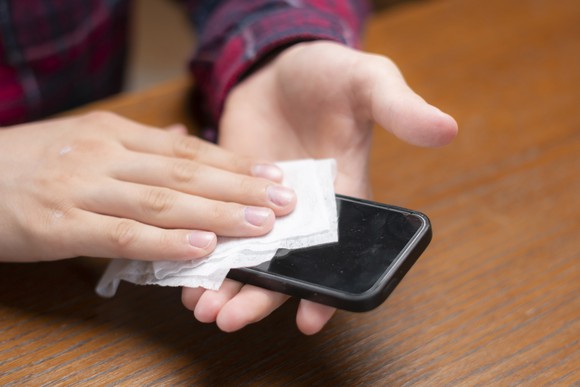 Closeup of hands wiping off a cell phone with a cloth. 