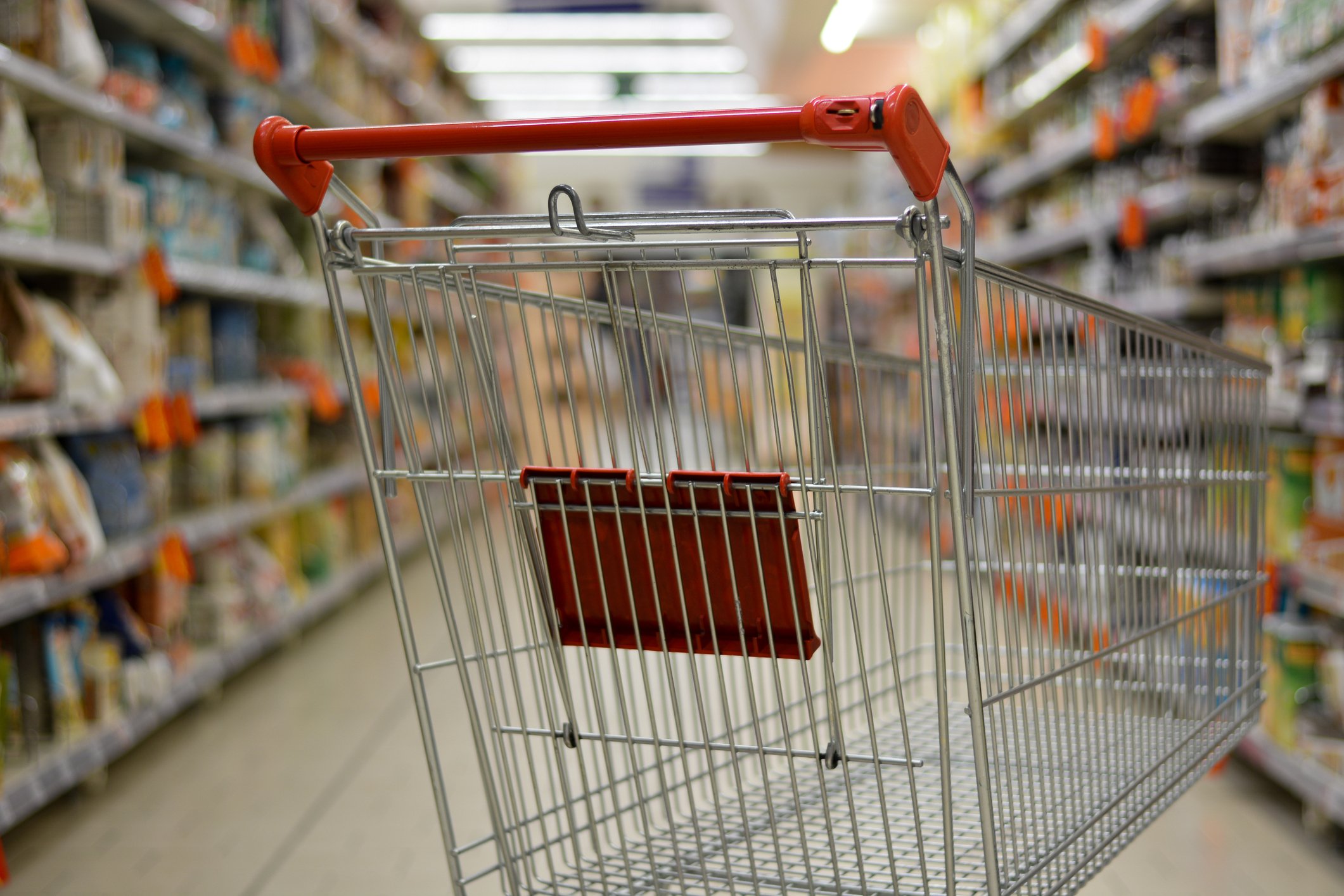 An empty shopping cart in a grocery store aisle.