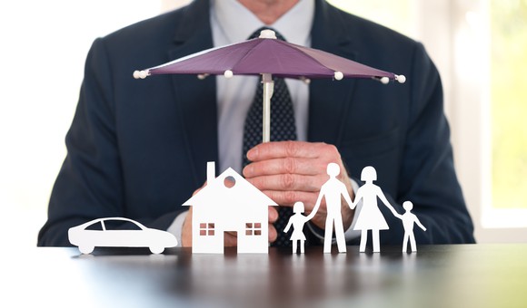 A man holding an umbrella over a paper cut out family, home, and car