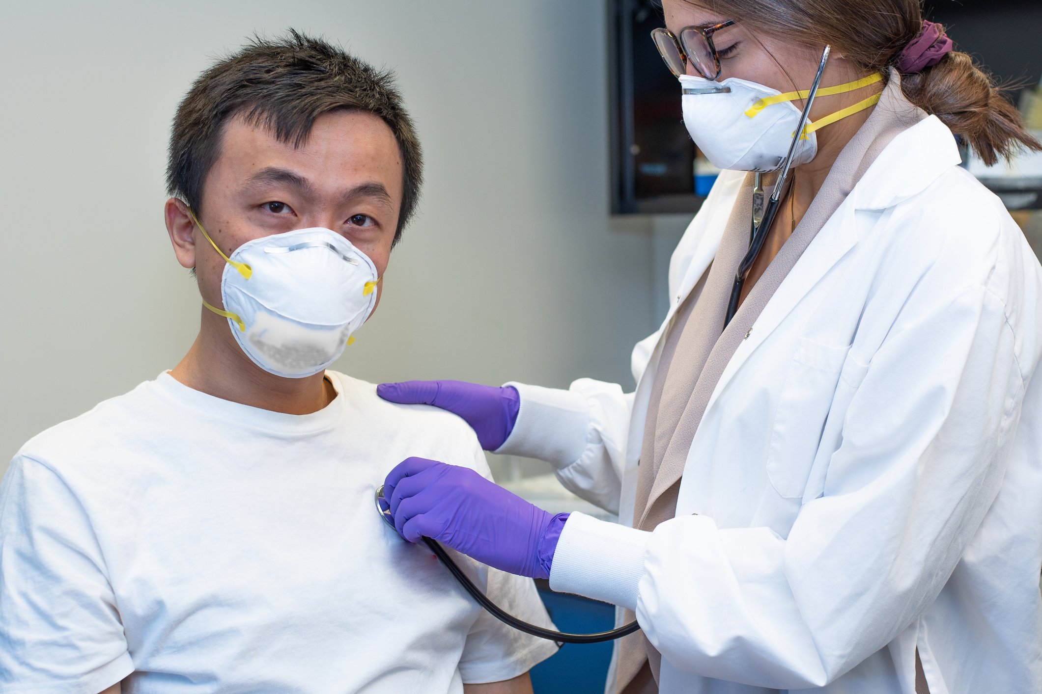 Masked doctor listening to the heart of a patient in a face mask
