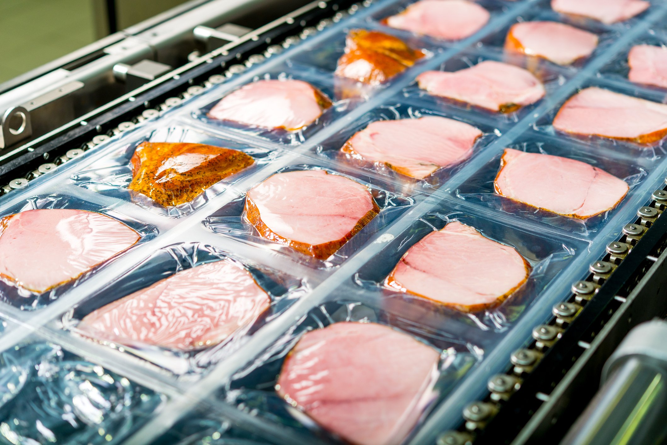 Ham being processed and packaged on an assembly line.