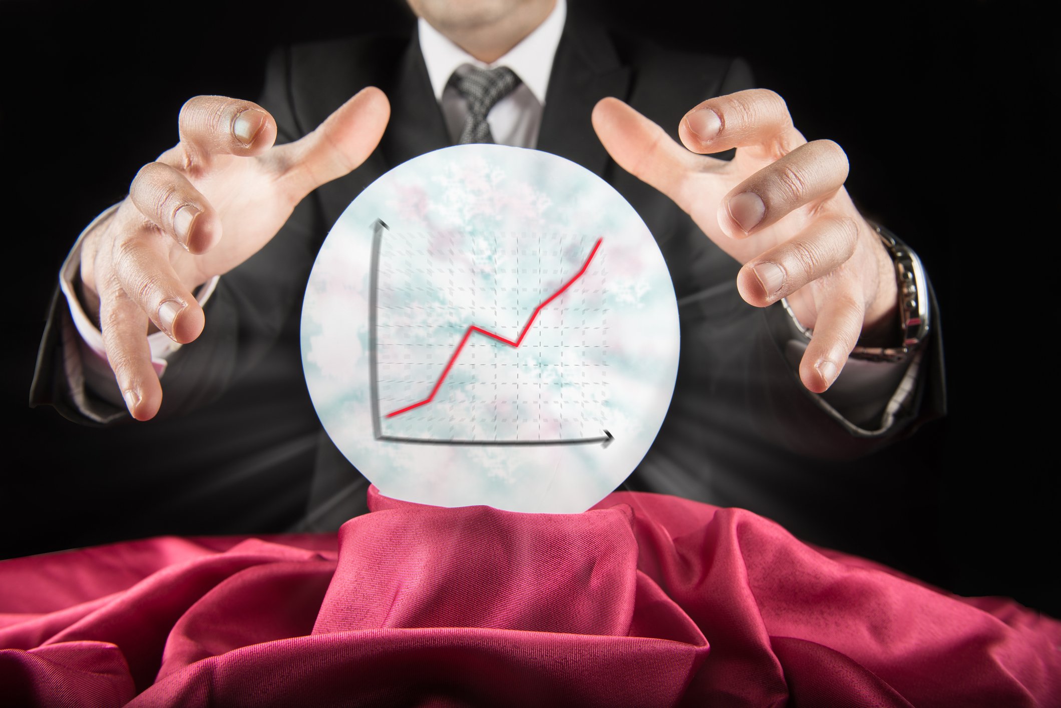 Fortune teller wearing a suit sees a rising graph in a crystal ball.