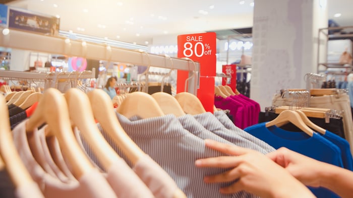 Hands picking through a rack of discounted shirts.