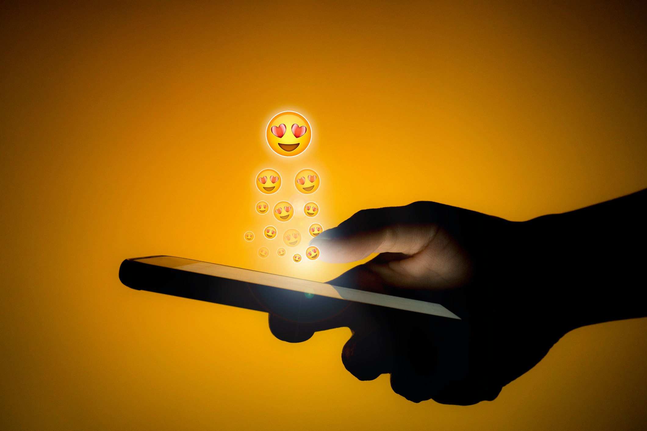 Emojis with heart-shaped eyes rise out a smartphone.