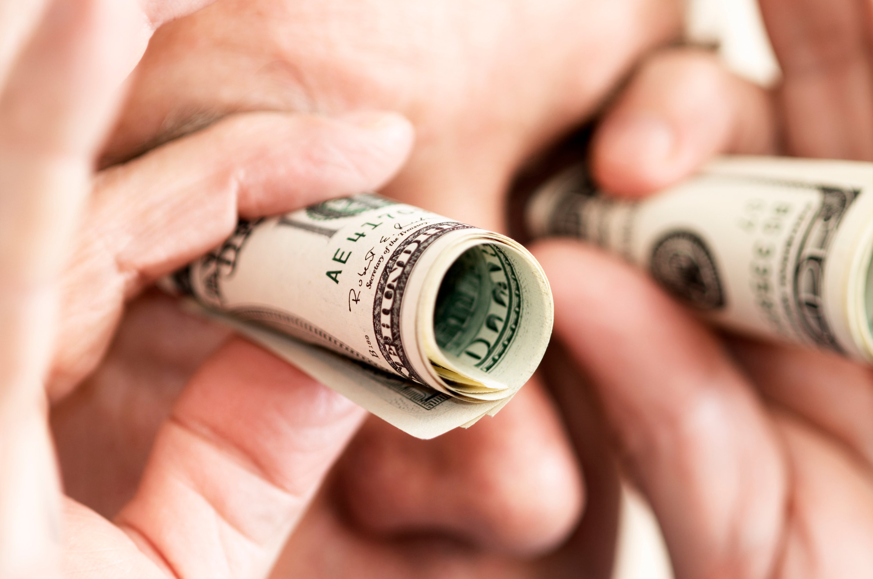 Man looking through rolled up cash like he has binoculars