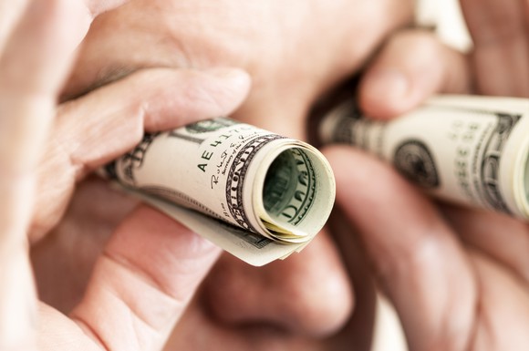 Man looking through rolled up cash like he has binoculars
