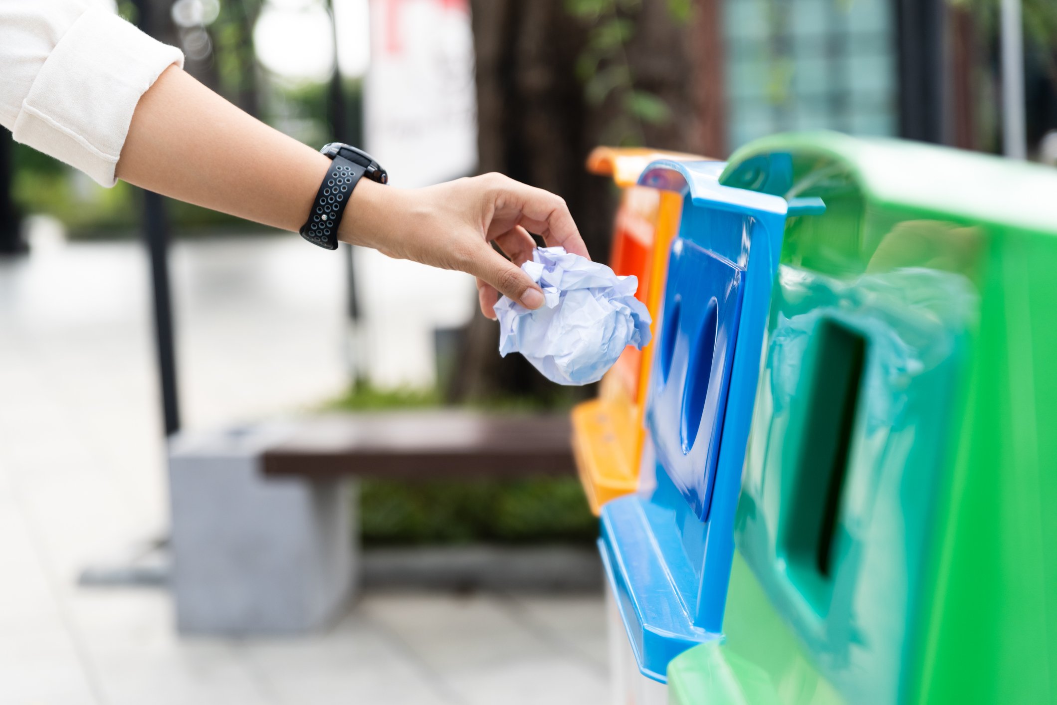 A woman throwing a crumpled paper in a recycling bin.