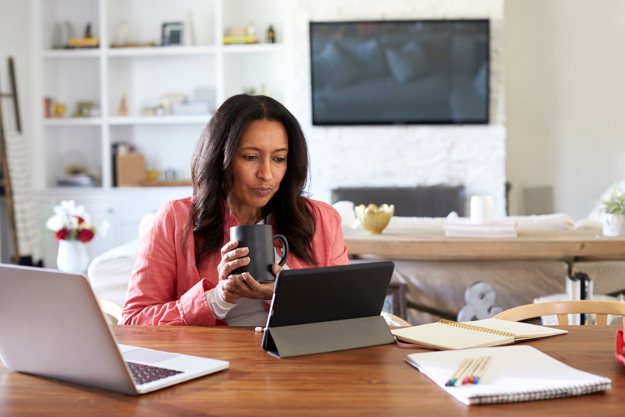 Woman looking at tablet; behind her is a living room with a wall unit and TV
