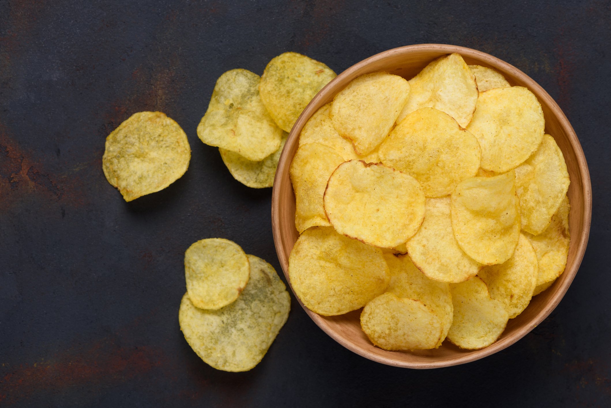 A bowl of chips on a wooden table with a few chips scattered around it.
