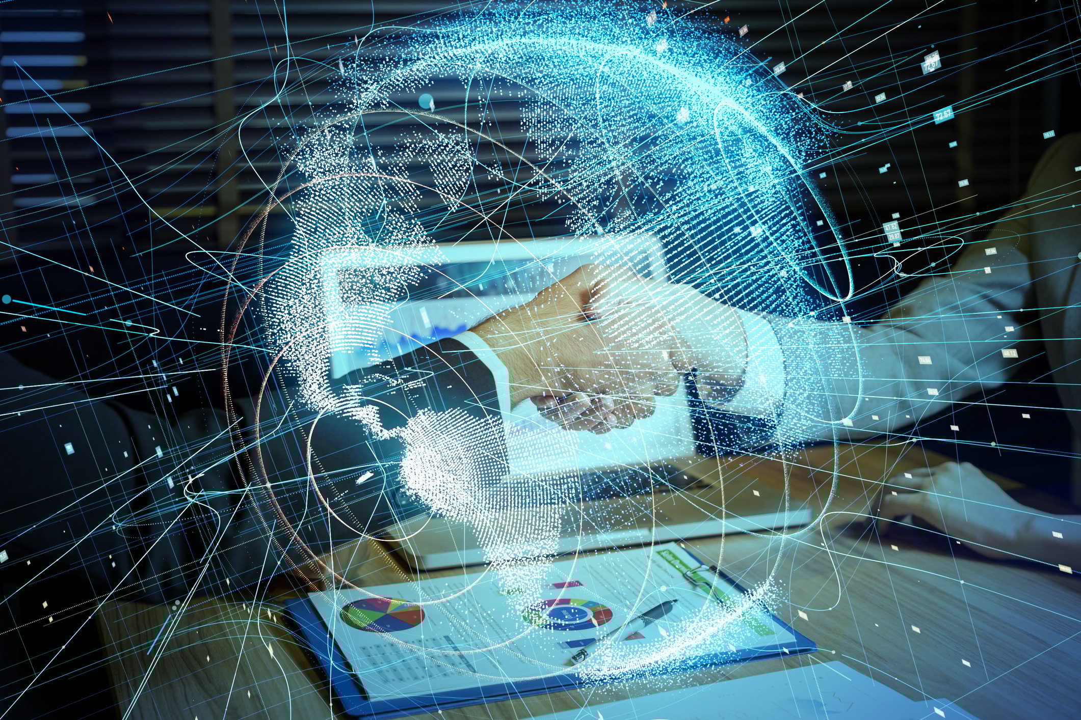 Two people shaking hands over table with laptop and papers