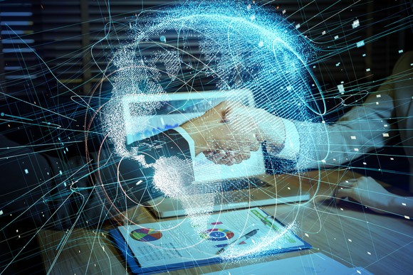 Two people shaking hands over table with laptop and papers