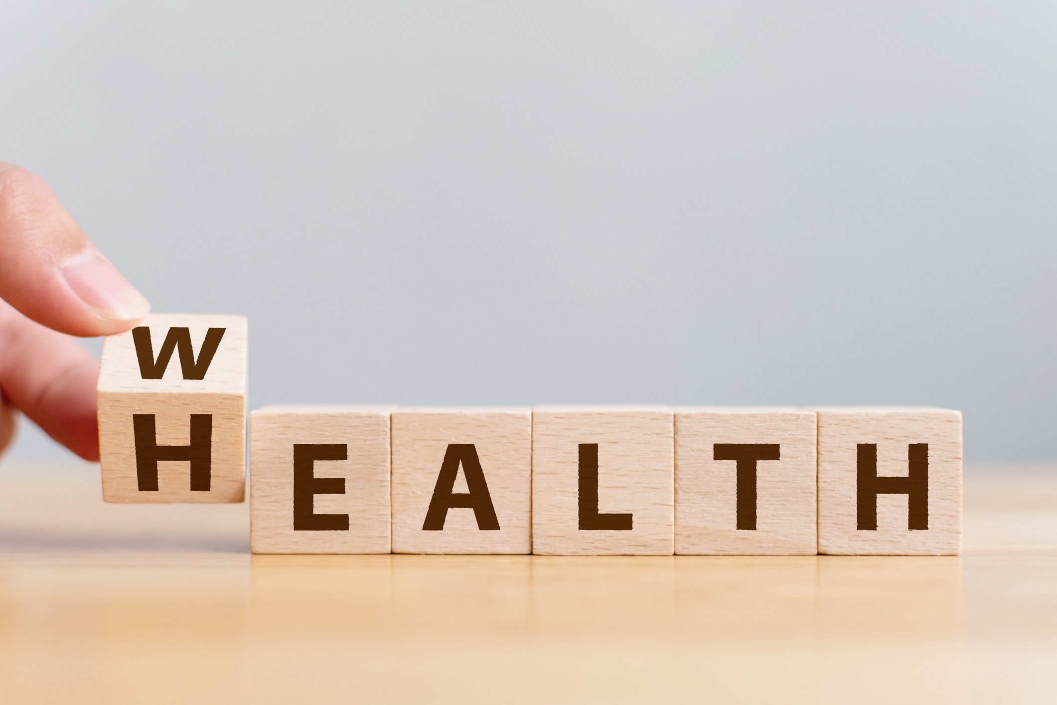 Wooden cubes with letters spelling health. Hand turning the first one to spell wealth