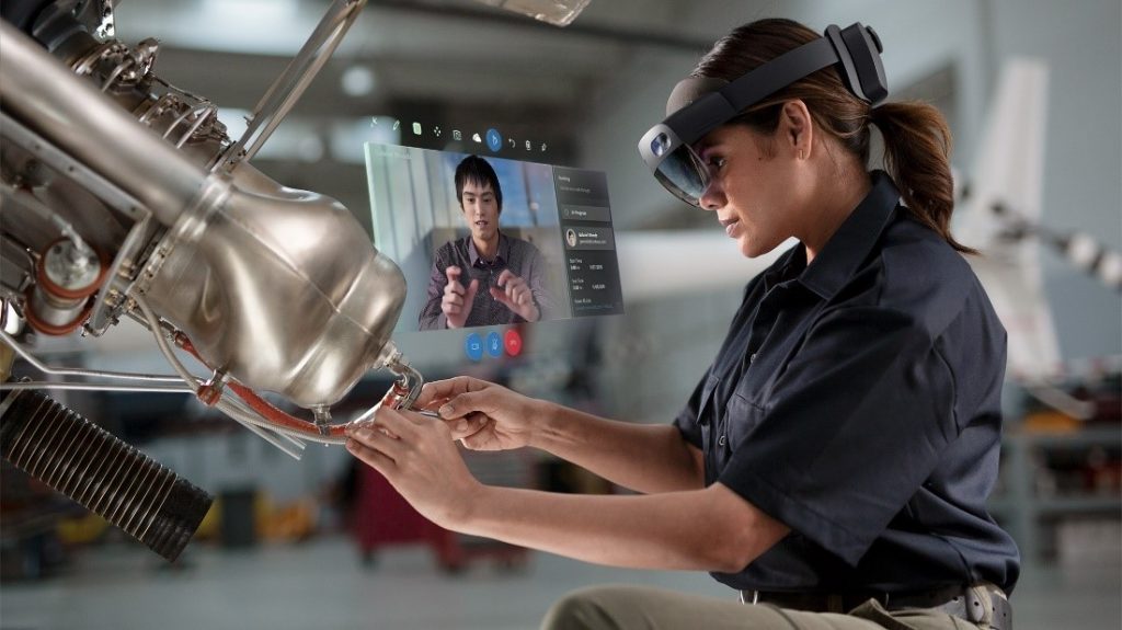 illustration shows the Microsoft HoloLens 2 being used by a factory worker as she produces a part.