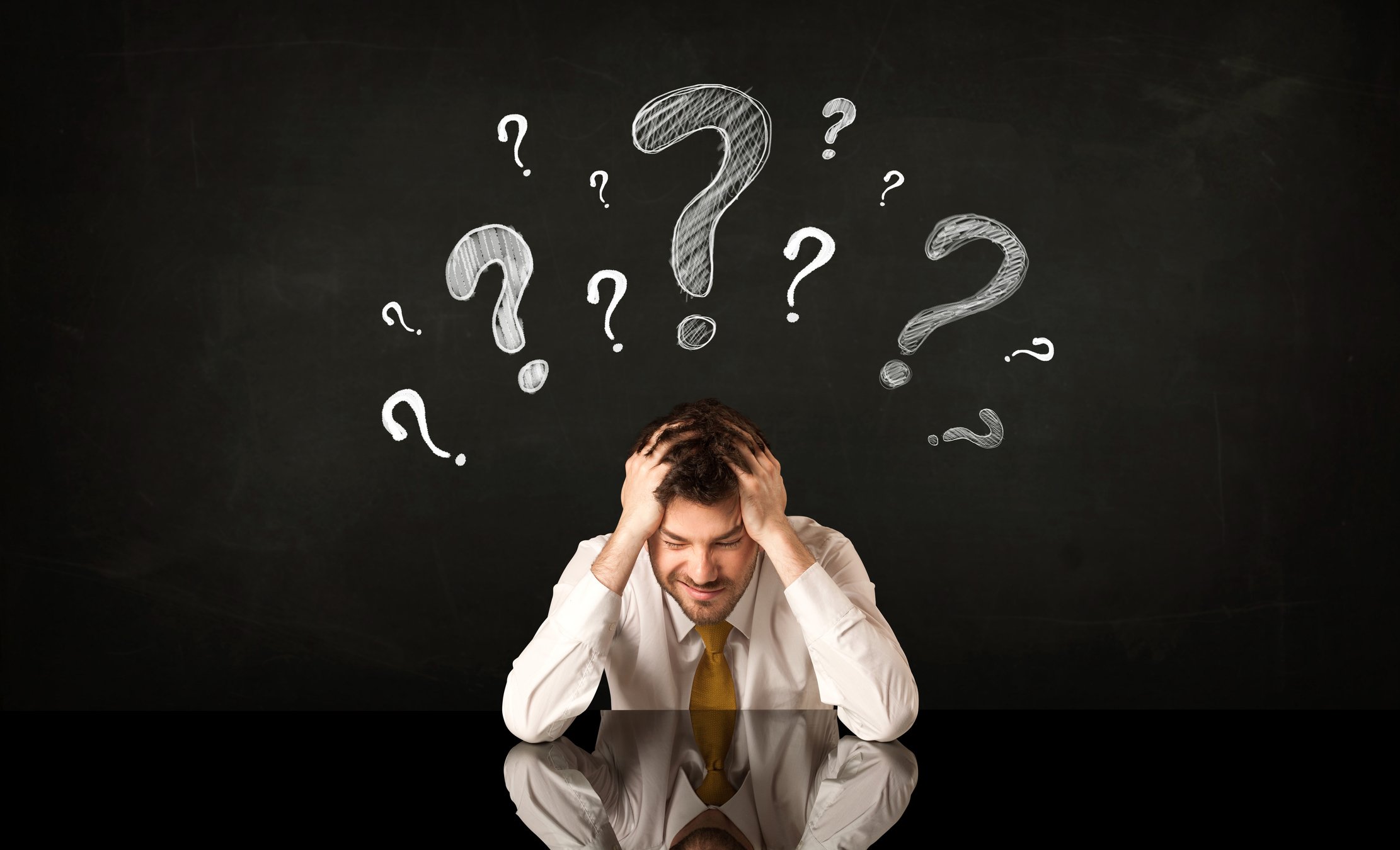 With his head in his hands, a businessman has question marks over his head.