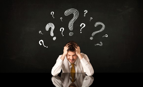 With his head in his hands, a businessman has question marks over his head.