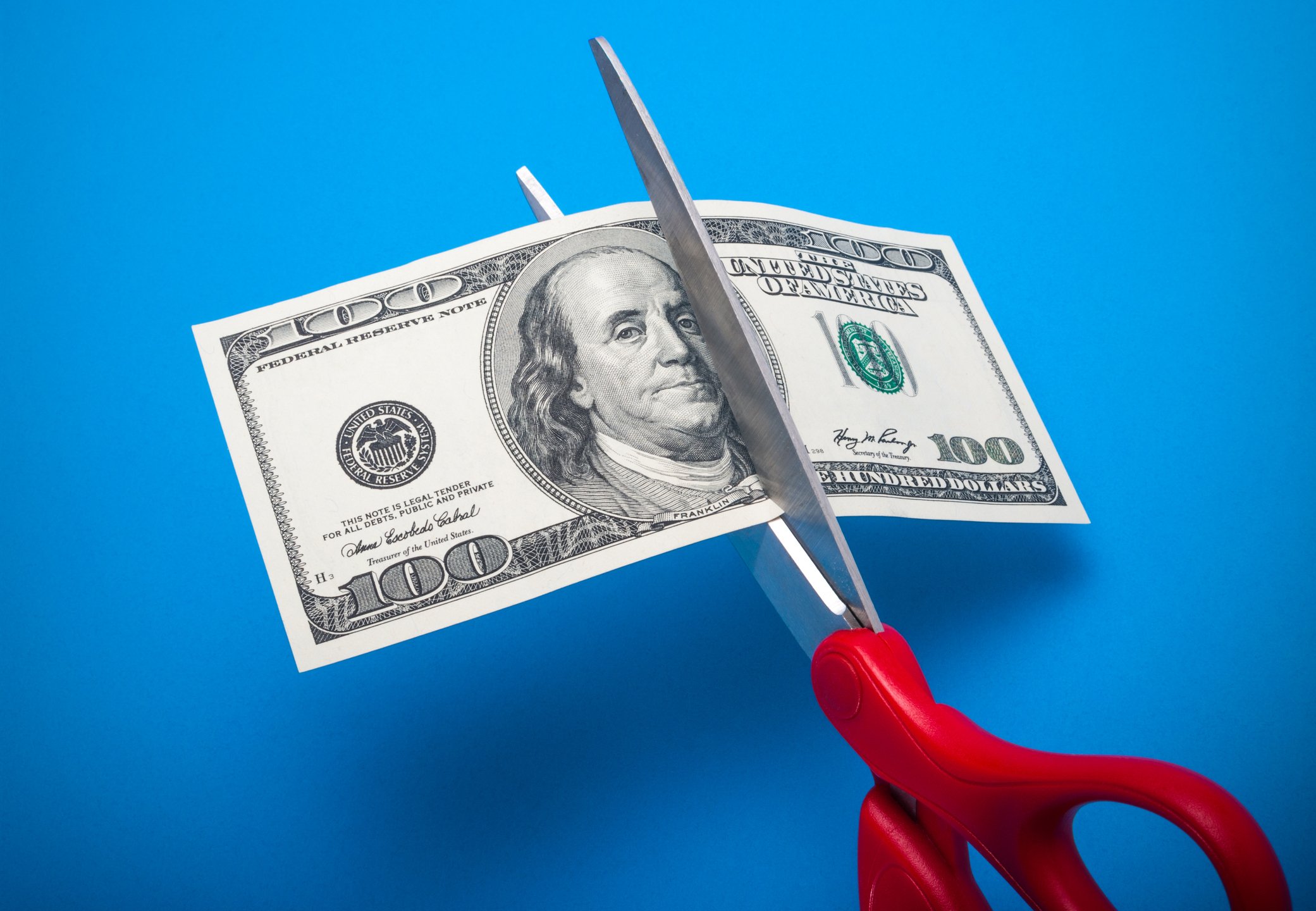 A pair of scissors cutting a hundred-dollar bill in half.