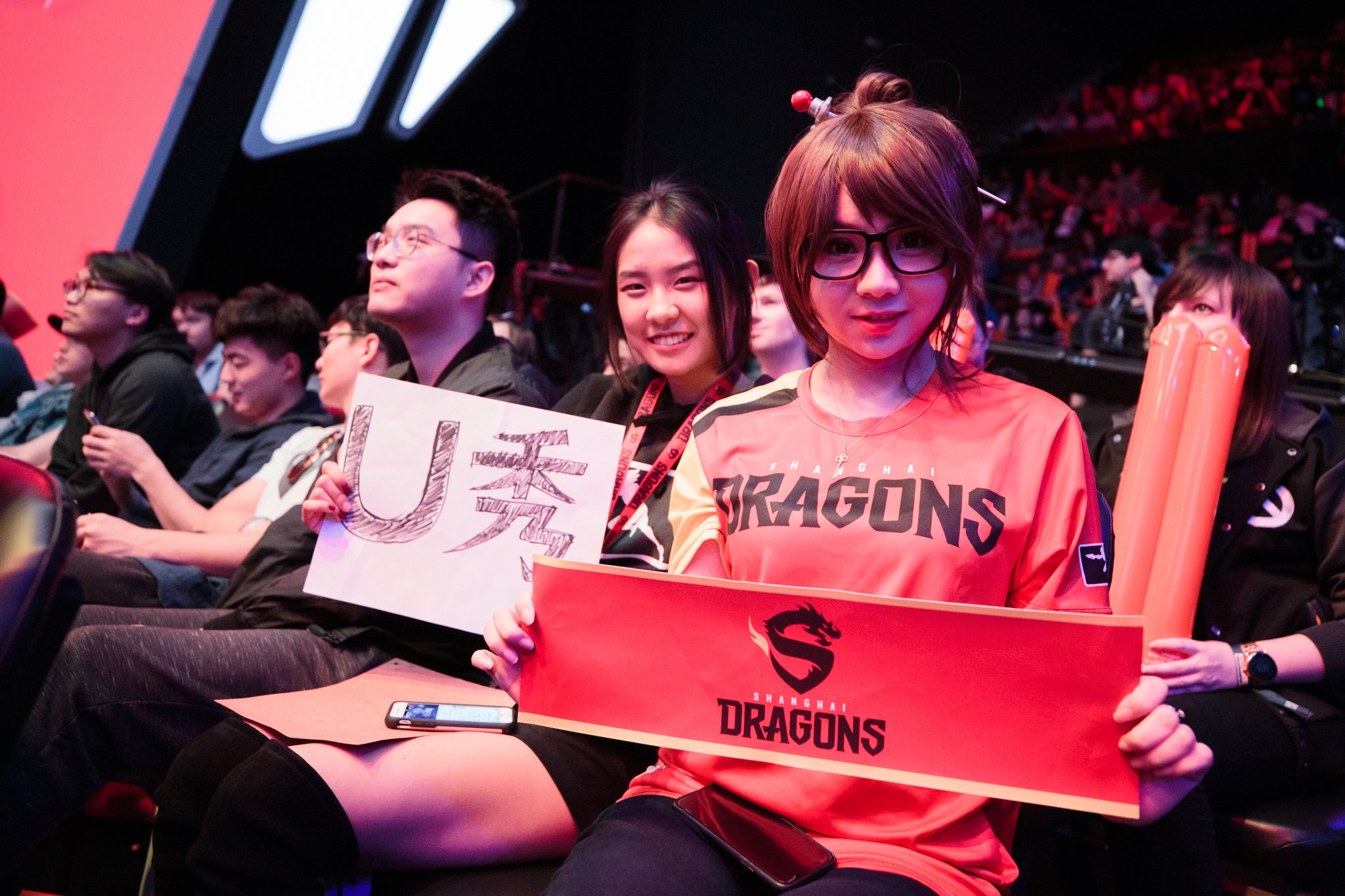 An Overwatch fan at a league match holding up a sign and wearing a team jersey for the Shanghai Dragons.