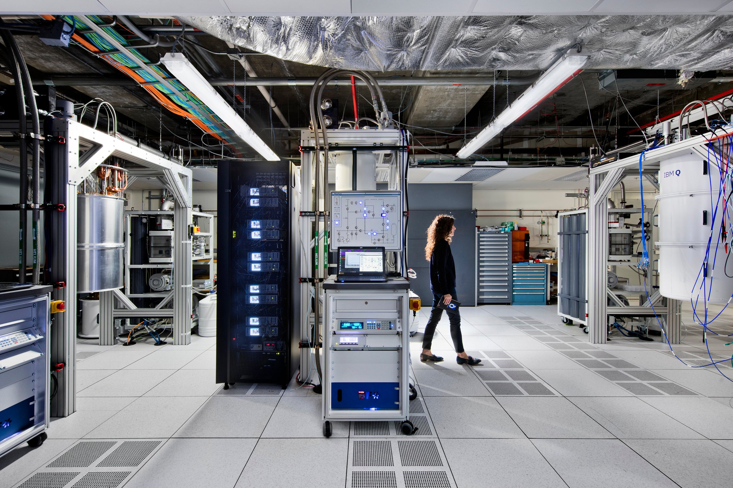 A woman walks through a modern data center, where many of the hardware racks are filled with quantum computing equipment.