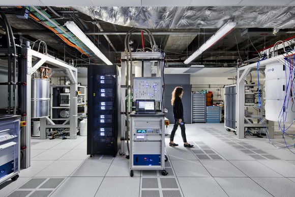 A woman walks through a modern data center, where many of the hardware racks are filled with quantum computing equipment.