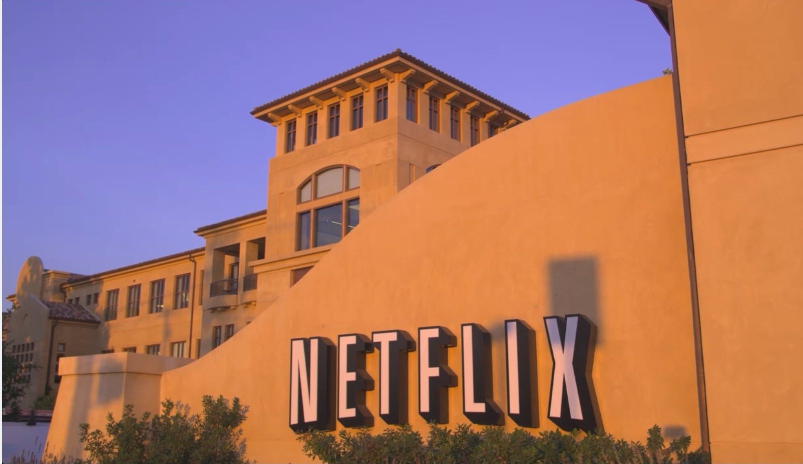 A white Netflix logo on a beige stucco wall outside the company's headquarters in Los Gatos, California.