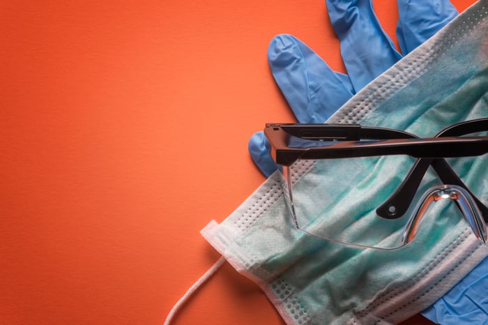 Gloves, face mask, and safety goggles on an orange background.