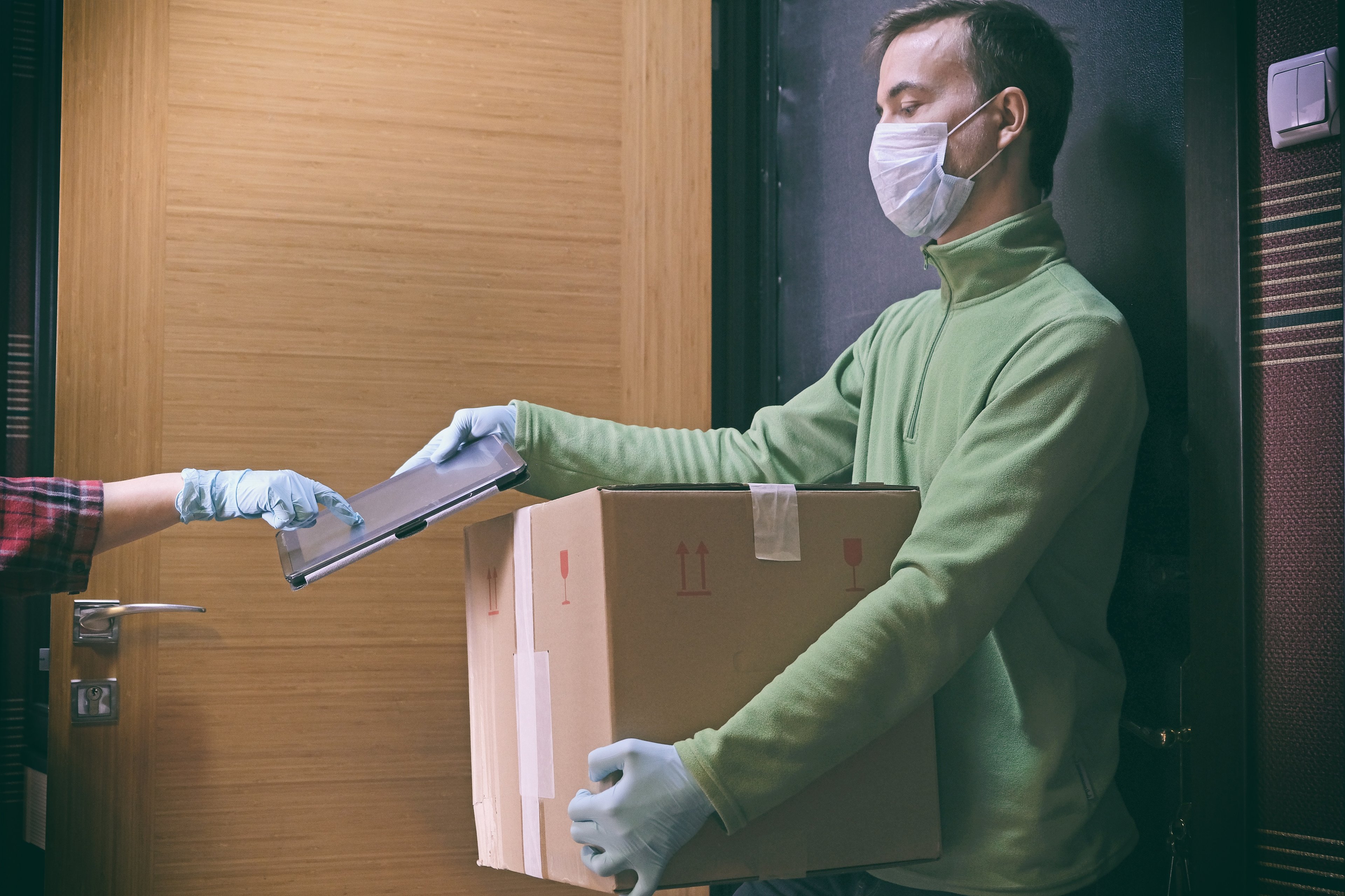 A man wearing a mask delivering a package to a person wearing gloves.