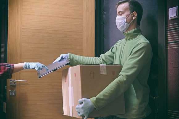 A man wearing a mask delivering a package to a person wearing gloves.