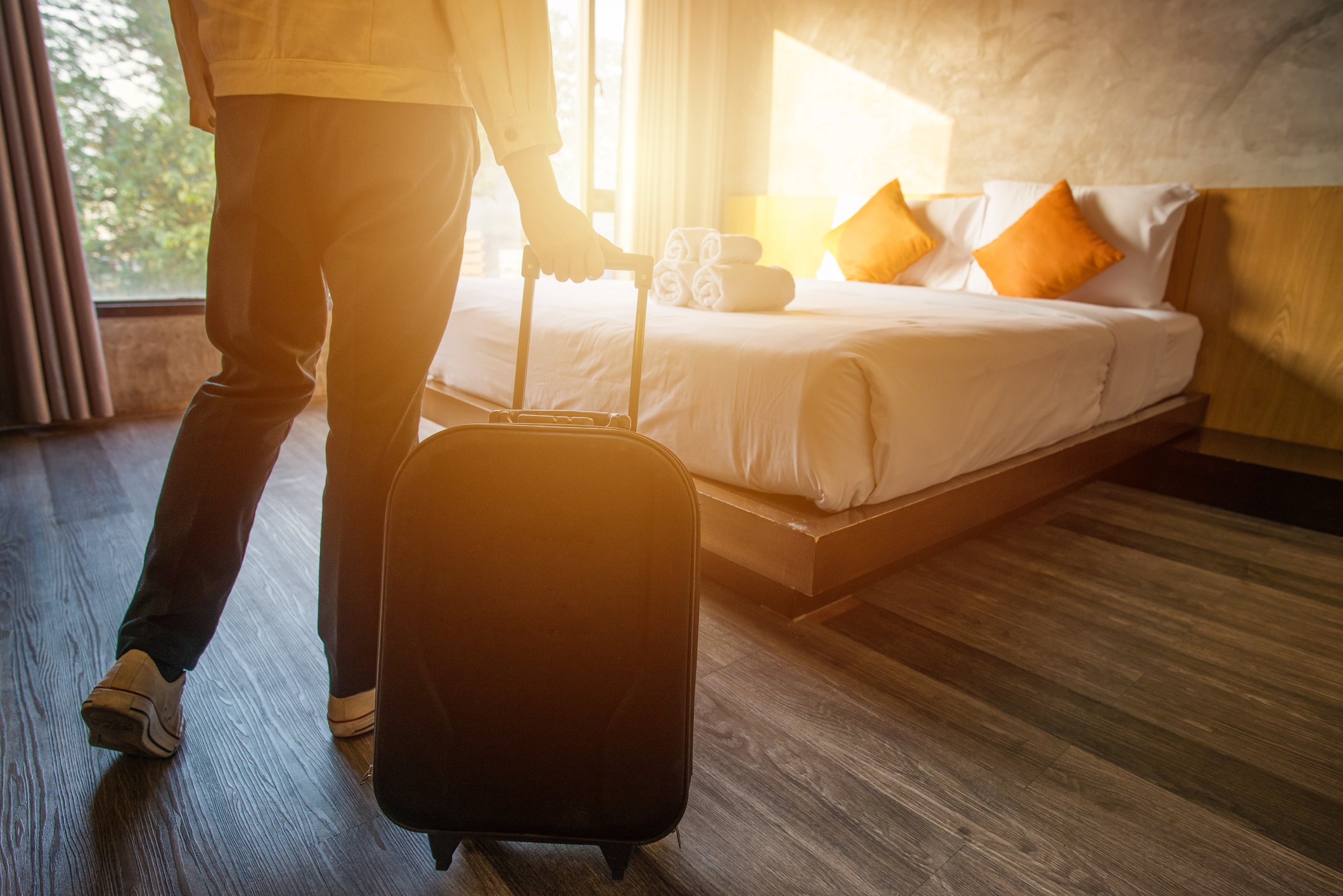 A person pulling a suitcase into a hotel room with the sun shining through the window.