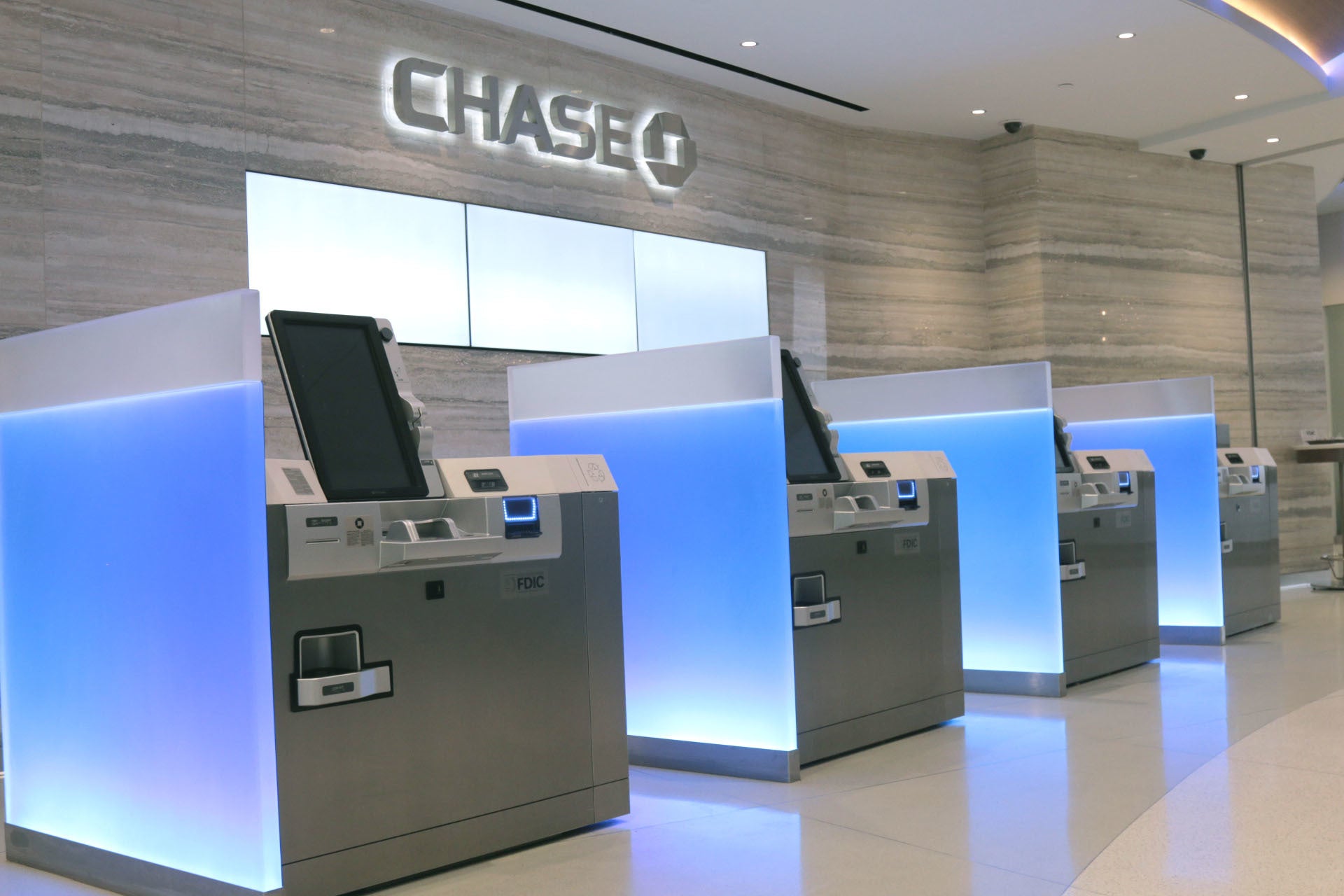 Automated teller machines at a Chase branch with marbled white floors and walls and the Chase logo.