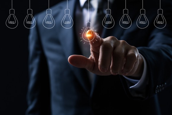 A man in a suit and tie pointing to a sketch of a light bulb