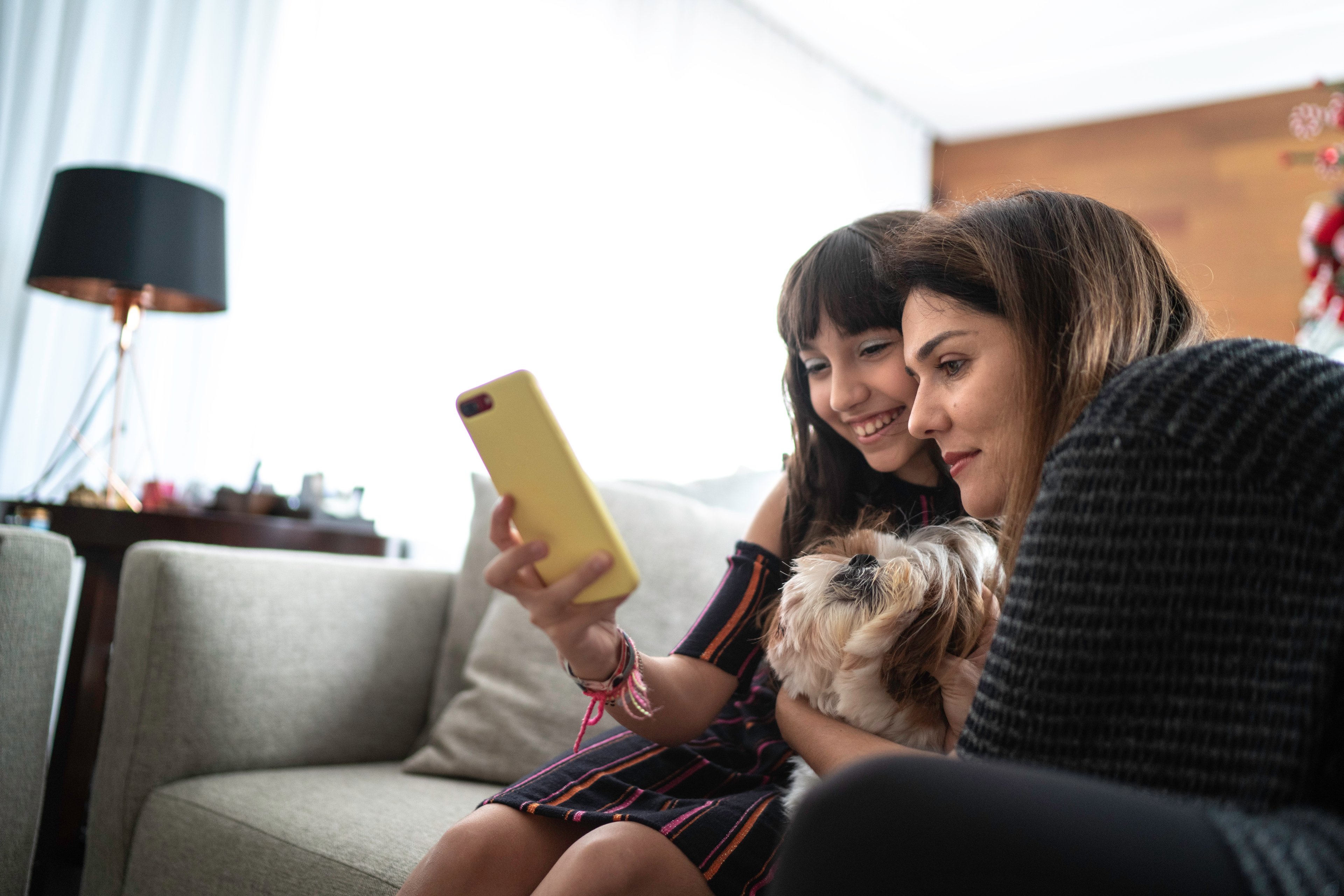 A woman with her daughter sitting on a couch and looking at an iPhone. 