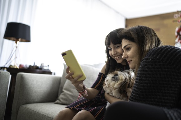 A woman with her daughter sitting on a couch and looking at an iPhone. 
