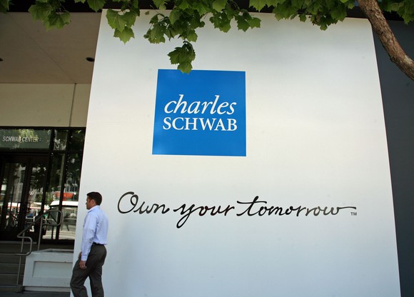 A man walking past Charles Schwab branding on a building.