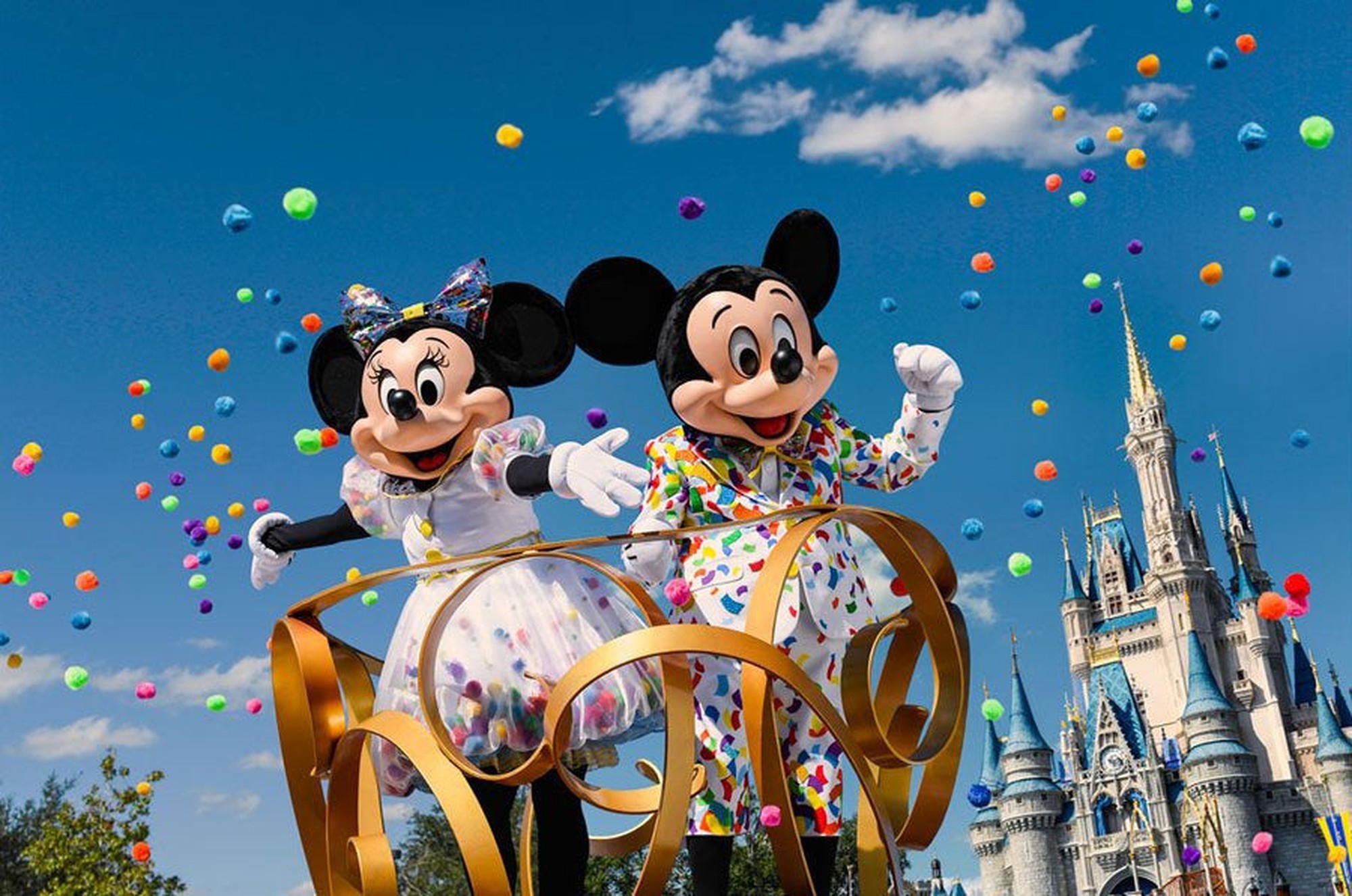 Minnie and Mickey Mouse on a parade float in Disney's Magic Kingdom under a shower of multi-colored balloons.