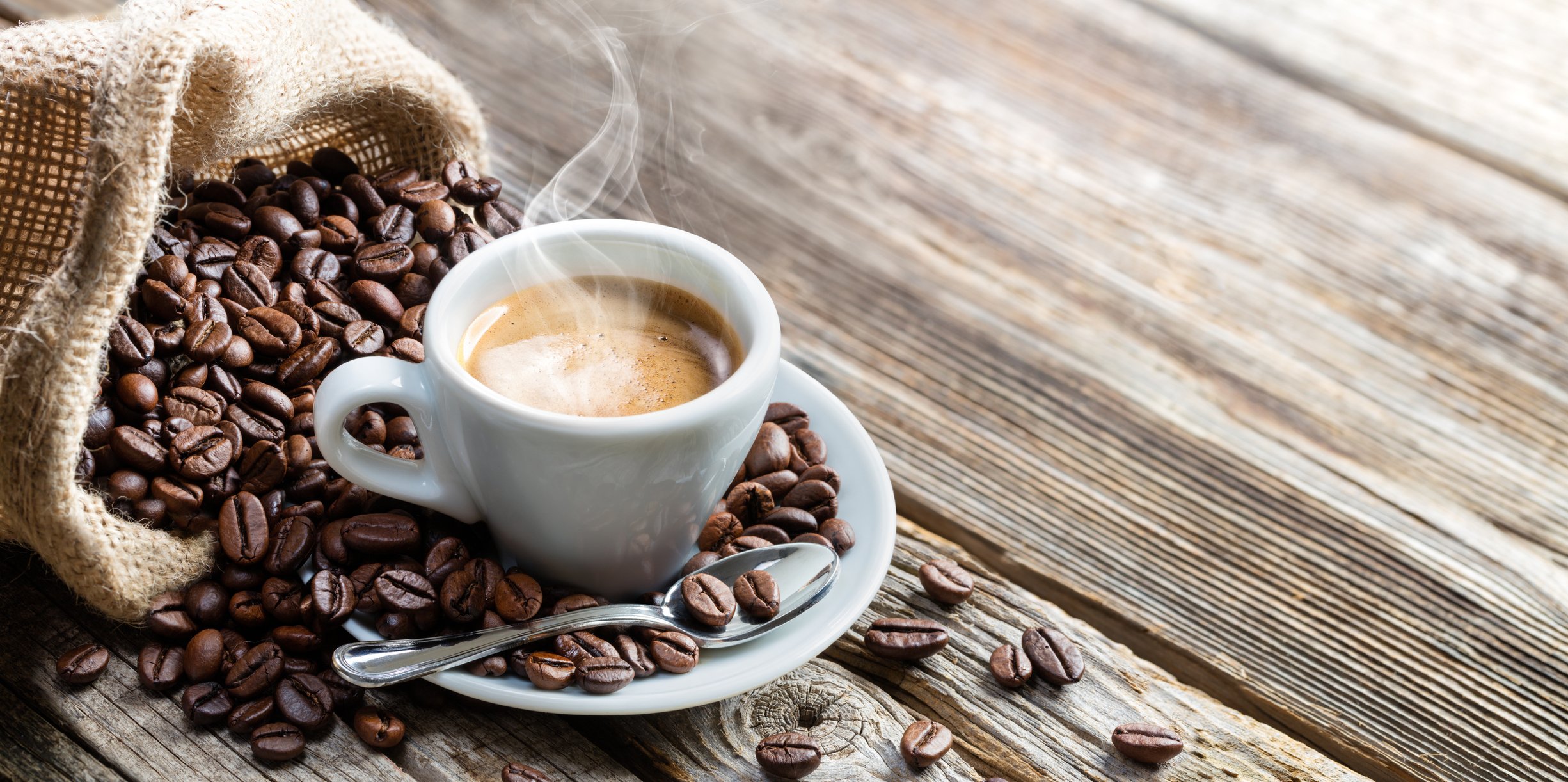 Cup of espresso on a saucer beside a bag of spilled coffee beans.