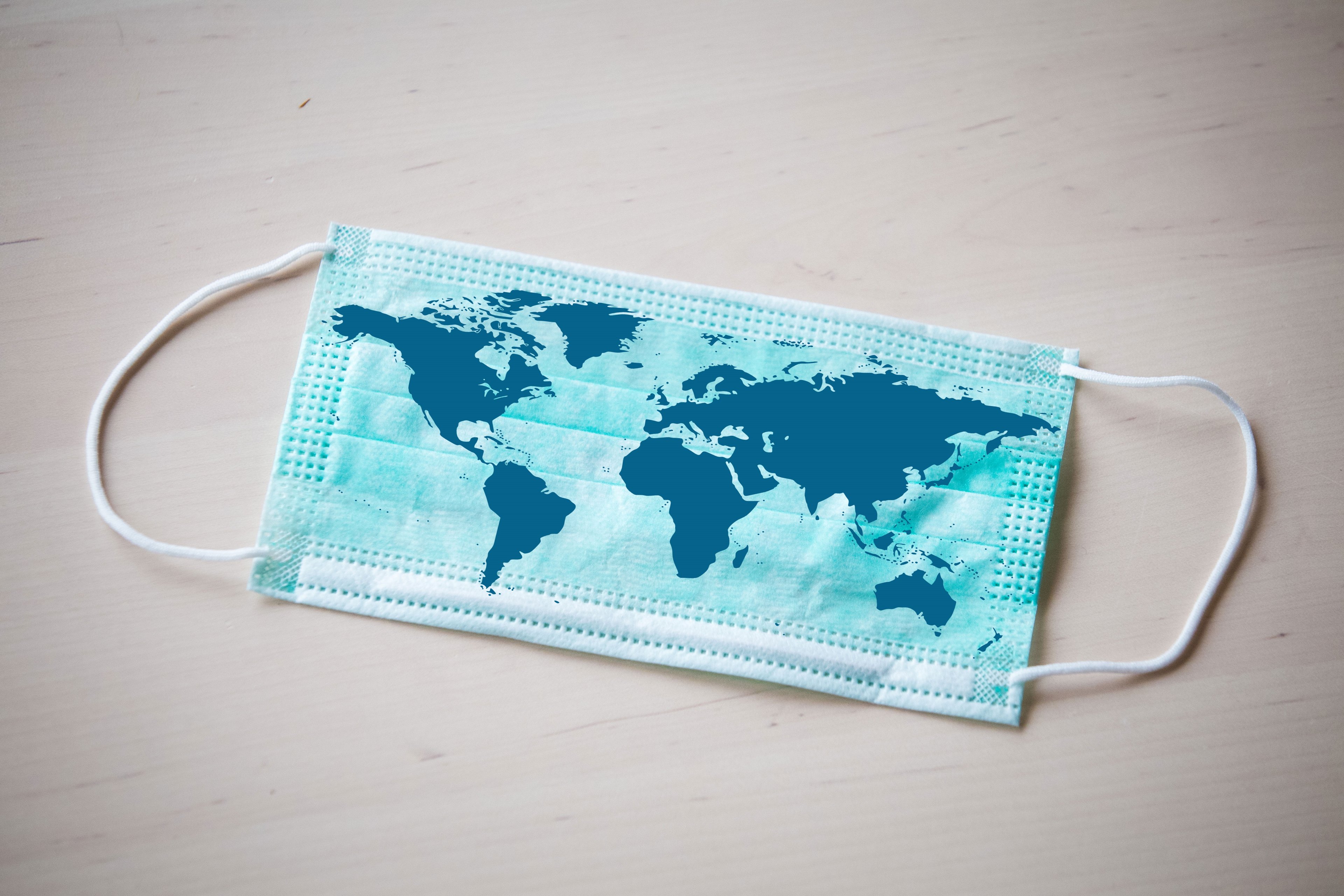 A light blue surgical mask with a map of parts of the world on it in navy. 