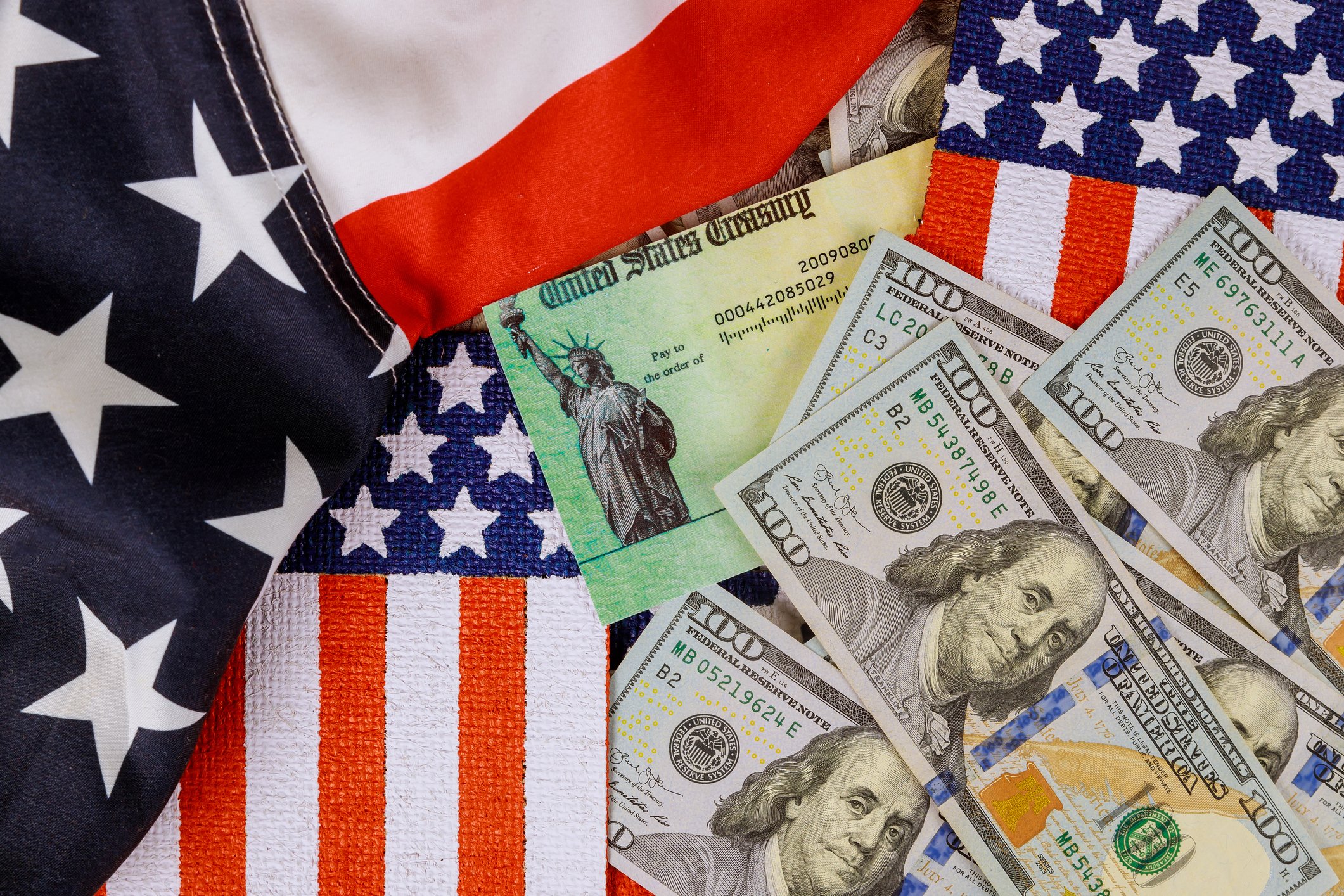 A stimulus check amid hundred-dollar bills and U.S. flags.