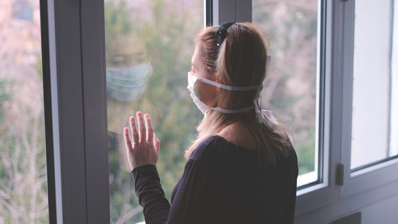 A woman wearing a facemask while staring out of a window.