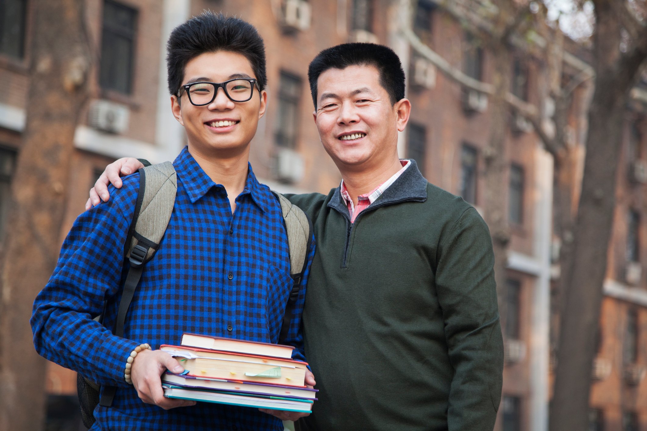 A parent embracing his son in front of a college dormitory.