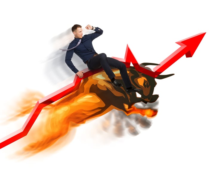 Man rides a bull up a rising stock arrow.