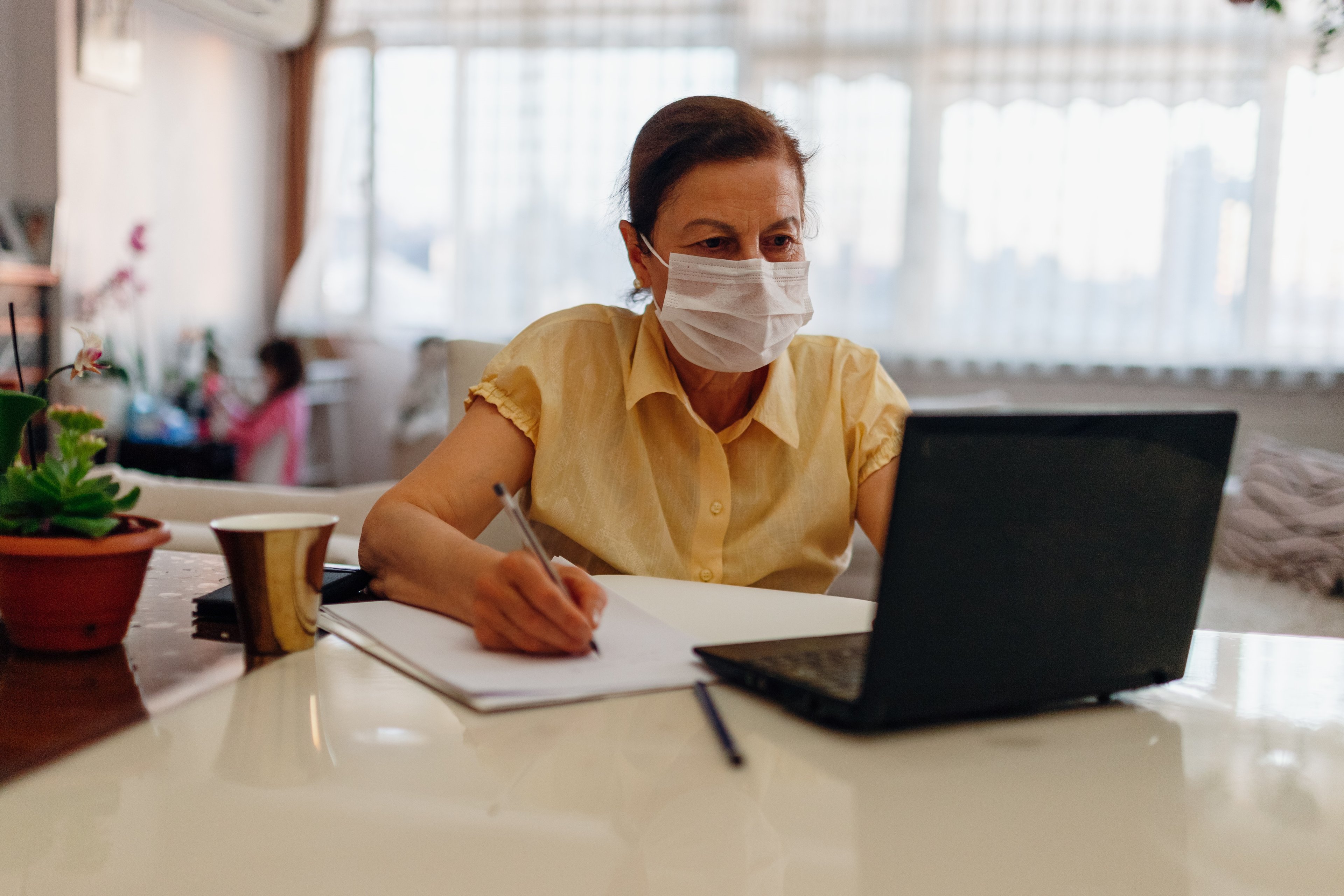 Woman working from home on her laptop wearing a mask. 