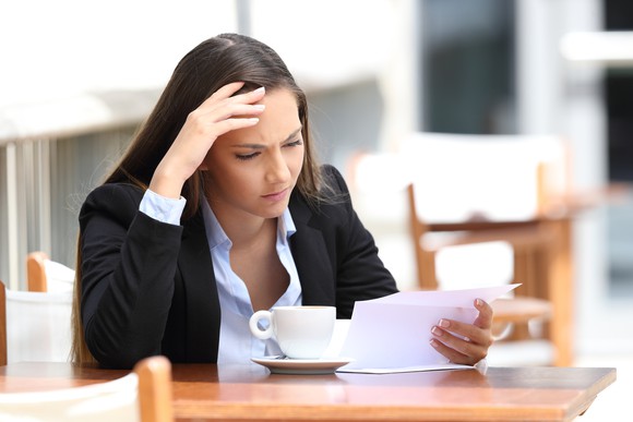 A woman with her head in her hand looks at a piece of paper.