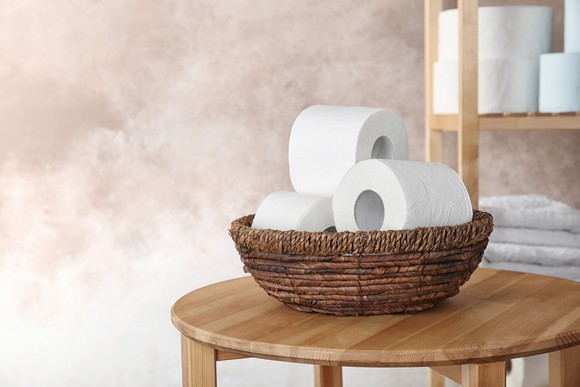 Straw bowl on wood table, filled with several toilet paper rolls