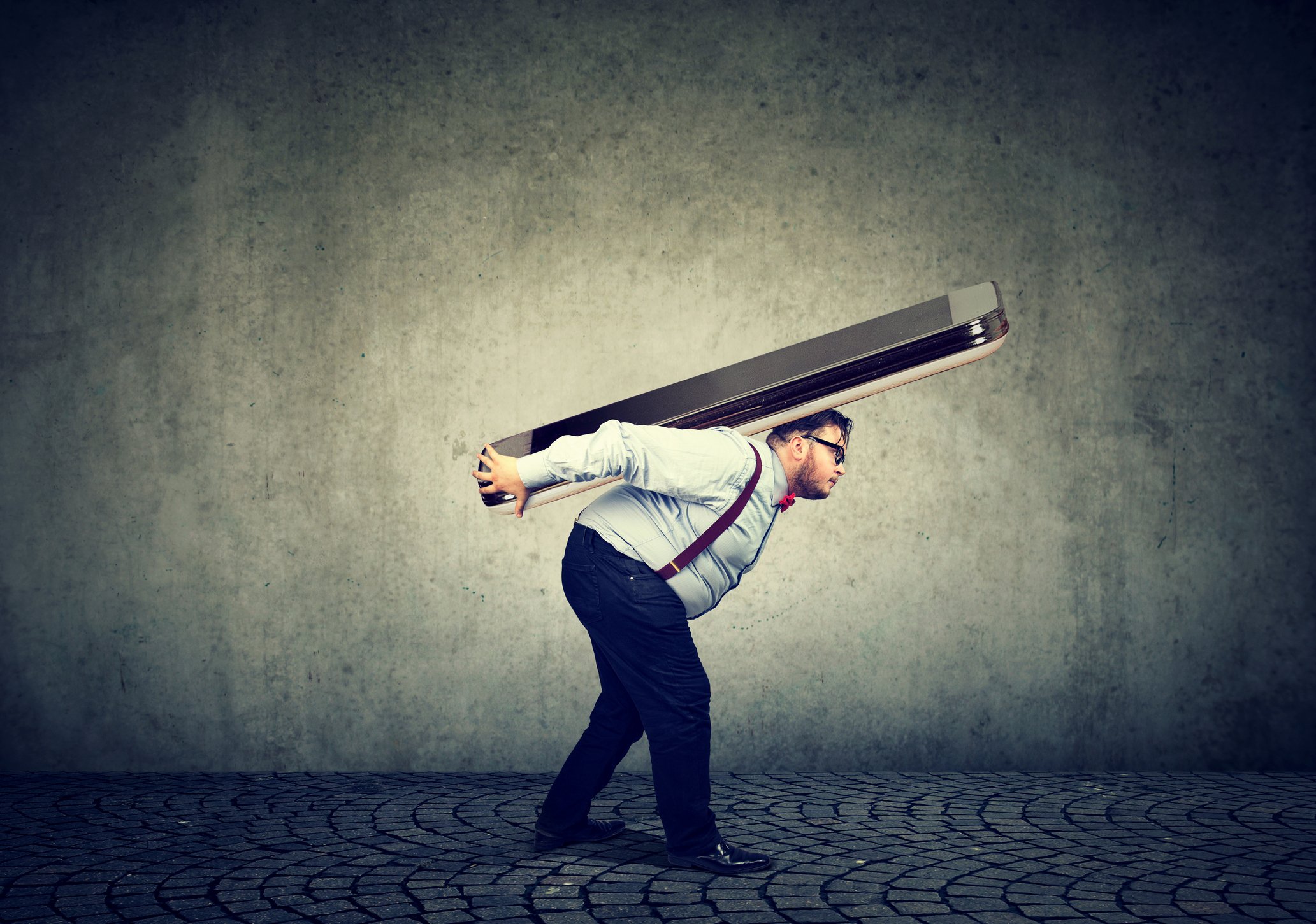 Man stooping under the weight of a giant smartphone on his back