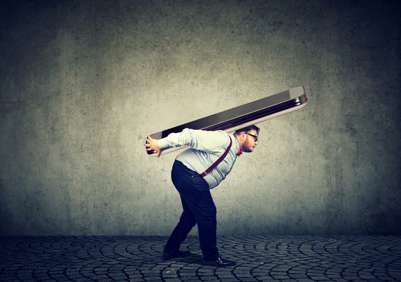 Man stooping under the weight of a giant smartphone on his back