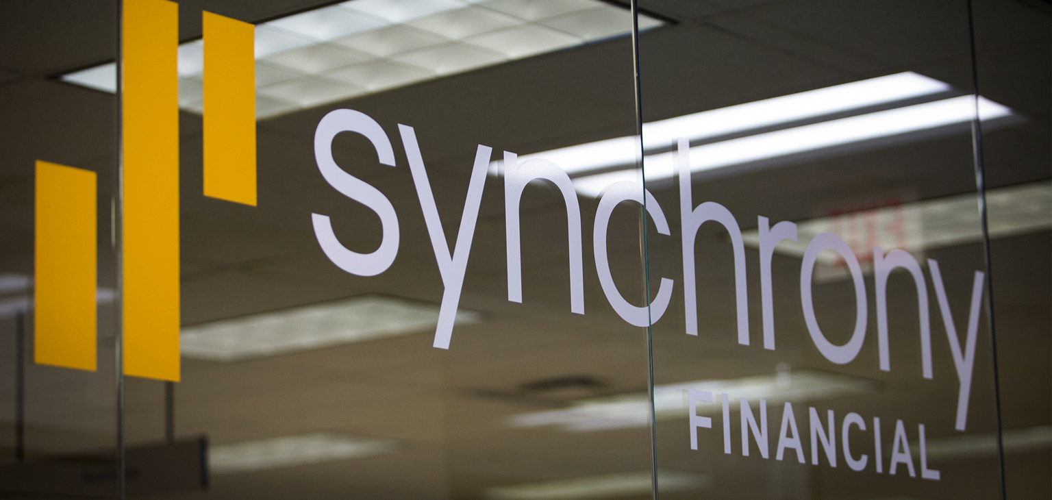Synchrony Financial logo on glass wall in office.