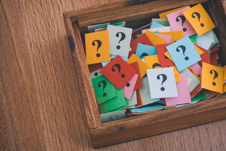 A wooden box full of note cards bearing question marks.