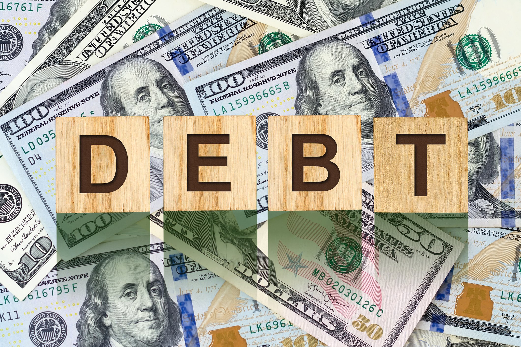 Wooden cubes spelling the word 'debt' on top of $100 bills.